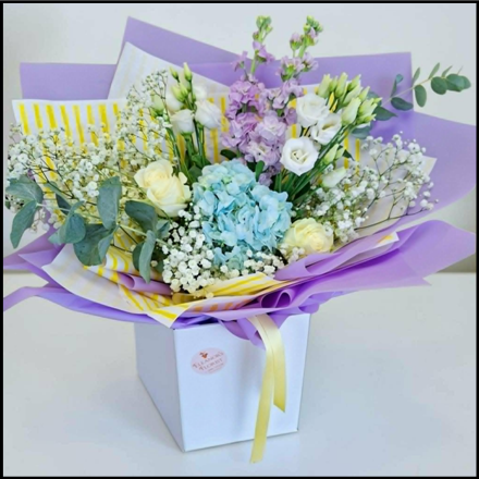 Bouquet of flowers wrapped in purple and white paper with a yellow ribbon on a white background