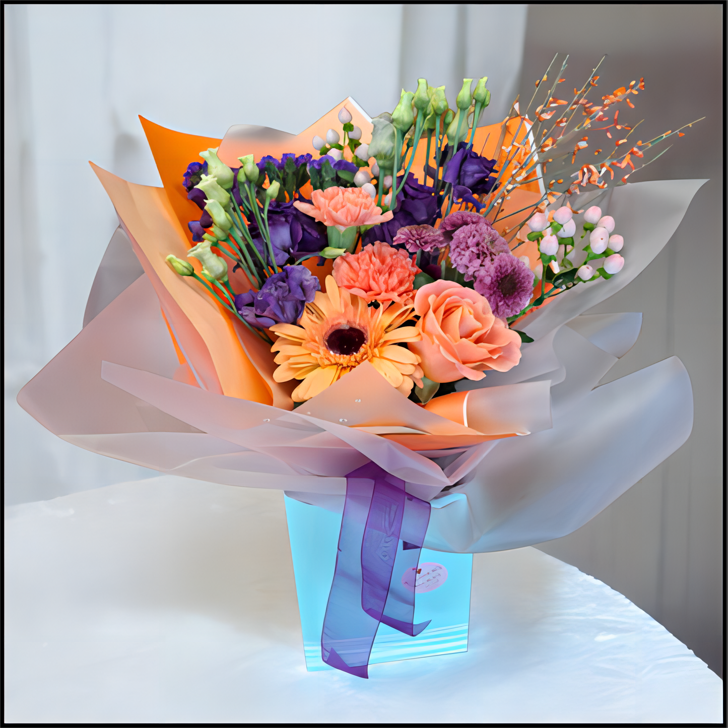 Bouquet of flowers wrapped in colourful paper with a purple ribbon, all in a cardboard box