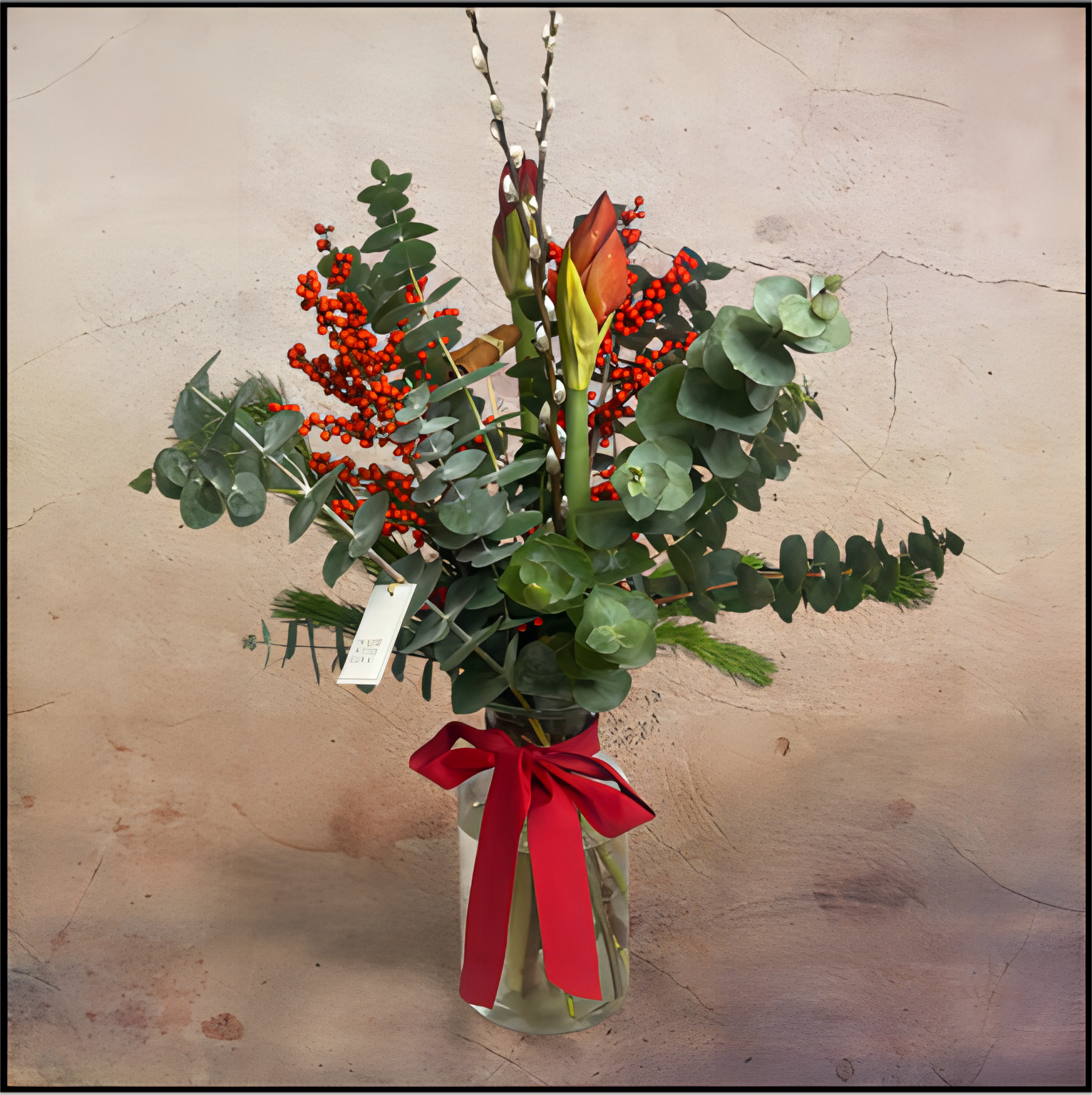 A timeless Christmas vase arrangement featuring two red Amaryllis as the focal point, surrounded by eucalyptus foliage, red berries and willow twigs. Tied with a satin ribbon, this natural and sophisticated design brings festive charm for the Christmas season